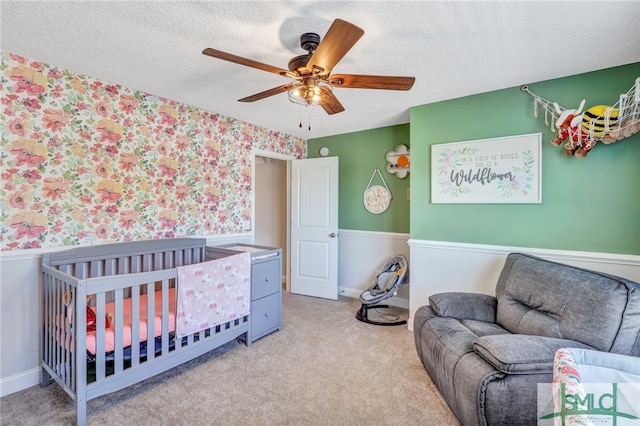 carpeted bedroom with a crib, ceiling fan, and a textured ceiling