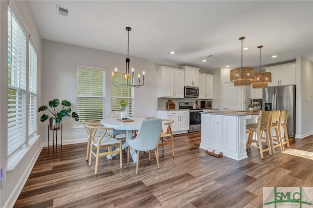 kitchen featuring an island with sink, decorative light fixtures, appliances with stainless steel finishes, and hardwood / wood-style floors