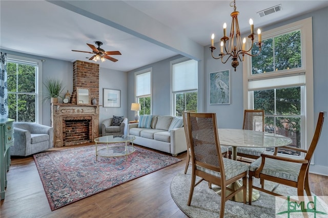 dining area with ceiling fan with notable chandelier, a fireplace, and hardwood / wood-style floors