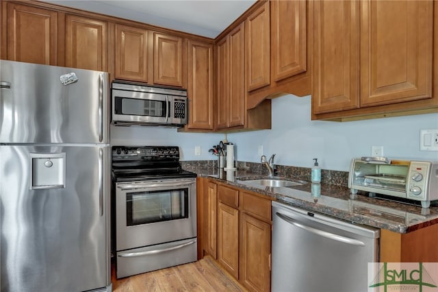 kitchen with sink, stainless steel appliances, light hardwood / wood-style floors, and dark stone counters