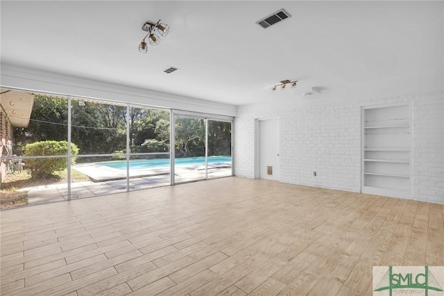 unfurnished living room featuring light hardwood / wood-style floors, built in features, and brick wall