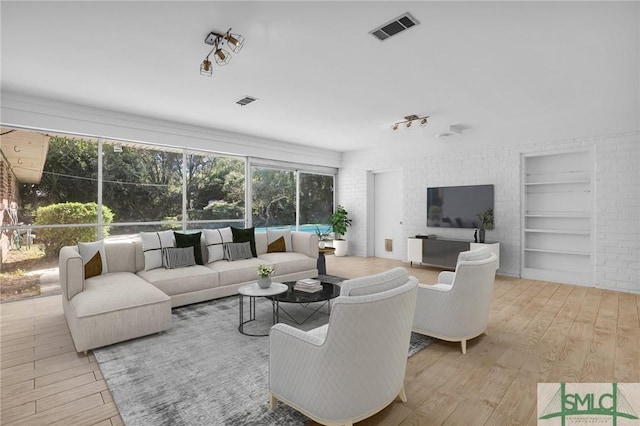 living room with built in features, brick wall, and light hardwood / wood-style flooring