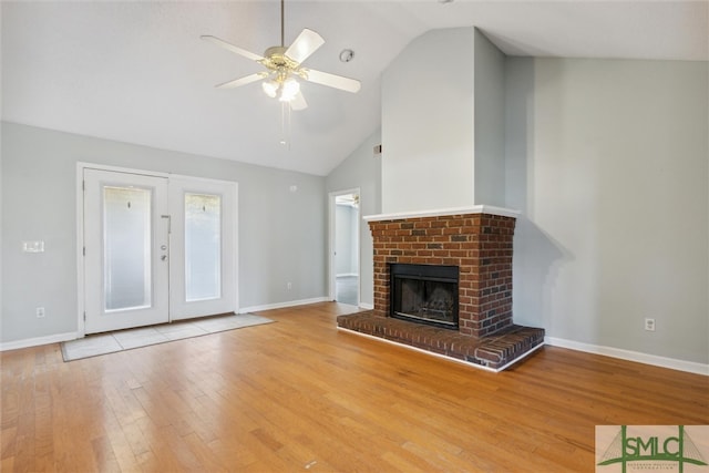 unfurnished living room with ceiling fan, high vaulted ceiling, a fireplace, light hardwood / wood-style floors, and french doors