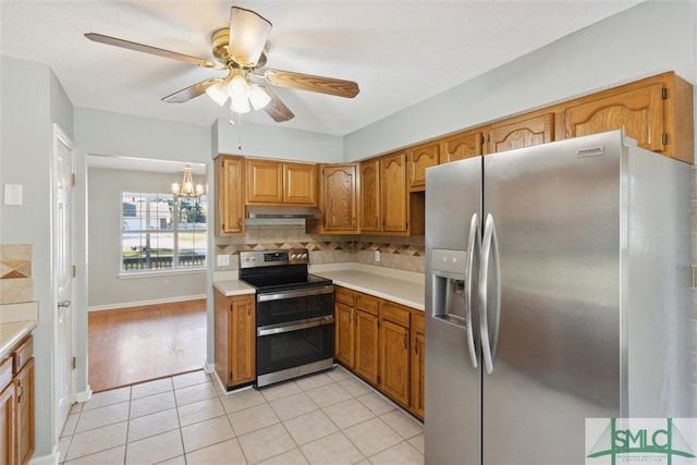 kitchen with light tile patterned flooring, stainless steel appliances, ceiling fan with notable chandelier, and backsplash