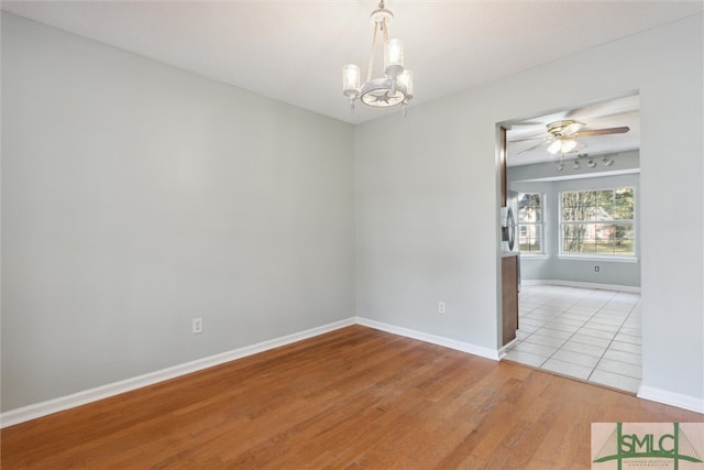 spare room featuring ceiling fan with notable chandelier and light wood-type flooring