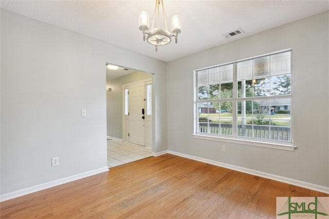 empty room with light hardwood / wood-style flooring and a notable chandelier