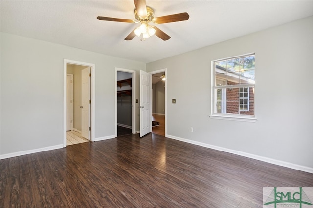 unfurnished bedroom with connected bathroom, dark wood-type flooring, a walk in closet, and ceiling fan