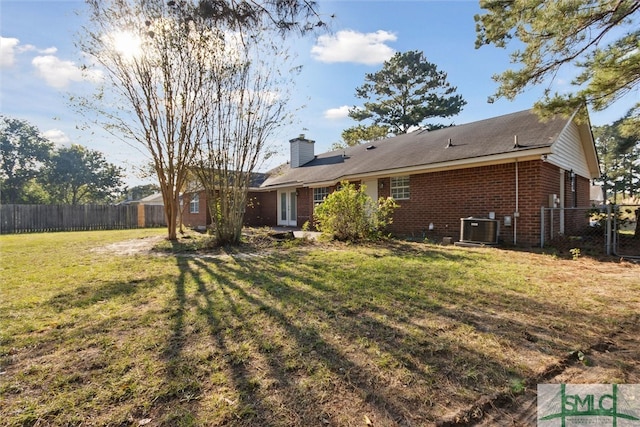 rear view of property with central air condition unit and a lawn