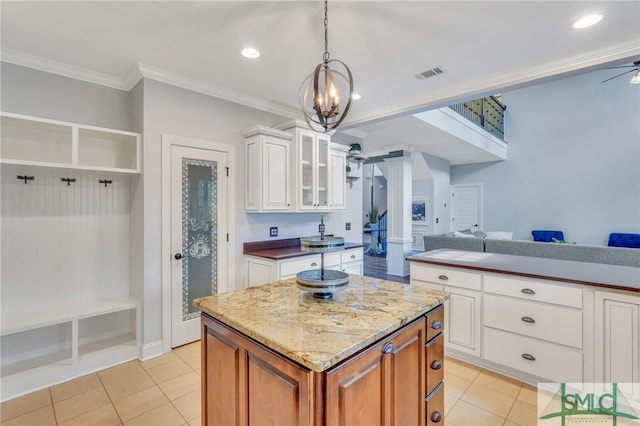 kitchen featuring white cabinets, light tile patterned floors, a kitchen island, crown molding, and decorative light fixtures