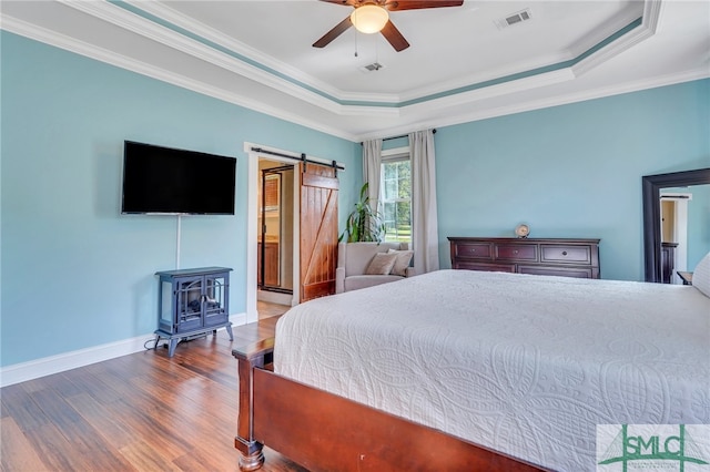 bedroom featuring wood-type flooring, a tray ceiling, ornamental molding, a barn door, and ceiling fan