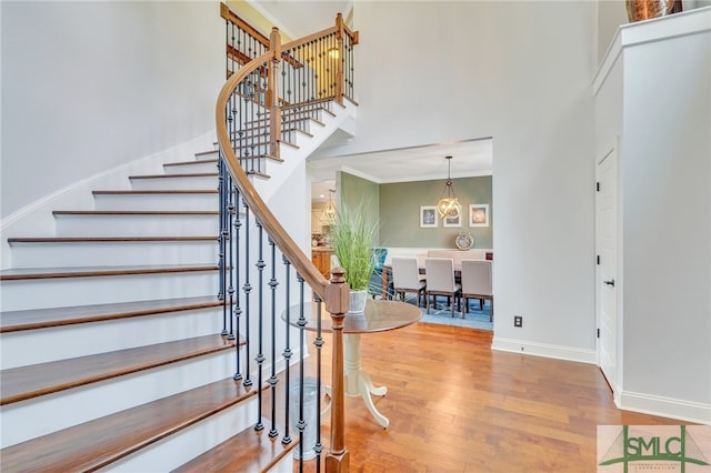 staircase with a notable chandelier, wood-type flooring, and a high ceiling