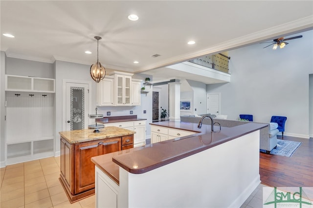 kitchen with hanging light fixtures, white cabinets, crown molding, light tile patterned floors, and a kitchen island with sink