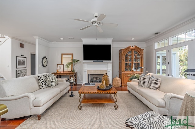 living room featuring wood-type flooring, ceiling fan, crown molding, and a tiled fireplace