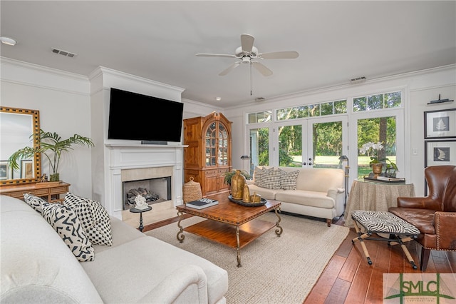 living room featuring a tile fireplace, french doors, crown molding, ceiling fan, and wood-type flooring