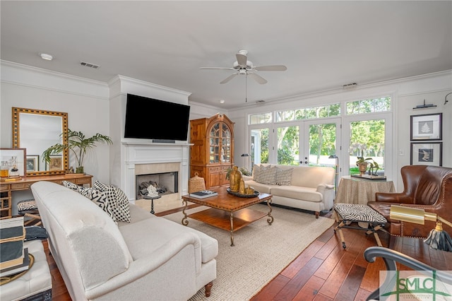 living room featuring french doors, hardwood / wood-style flooring, ceiling fan, ornamental molding, and a fireplace