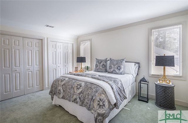 carpeted bedroom featuring ornamental molding and two closets