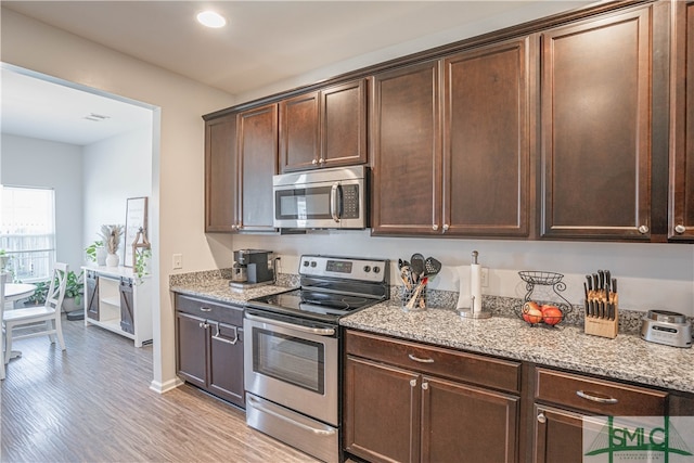 kitchen featuring light hardwood / wood-style floors, appliances with stainless steel finishes, light stone counters, and dark brown cabinets