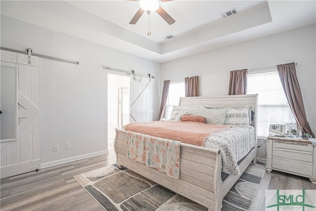 bedroom with hardwood / wood-style floors, a barn door, a raised ceiling, and ceiling fan