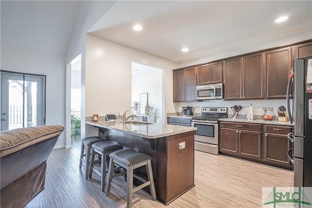 kitchen featuring appliances with stainless steel finishes, a kitchen bar, sink, light hardwood / wood-style floors, and light stone counters