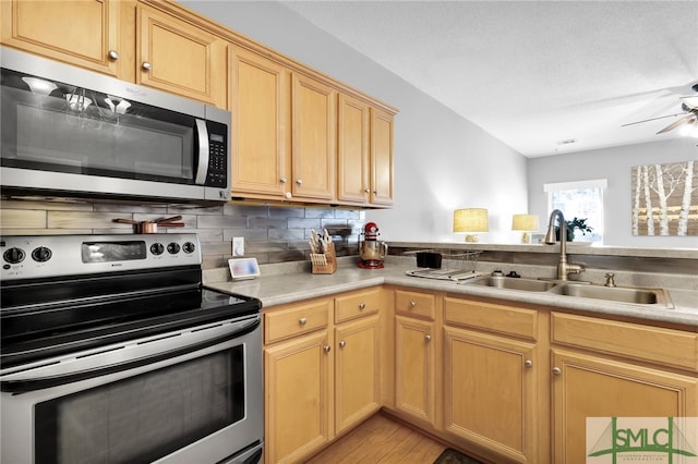 kitchen with appliances with stainless steel finishes, sink, light brown cabinetry, decorative backsplash, and light hardwood / wood-style flooring