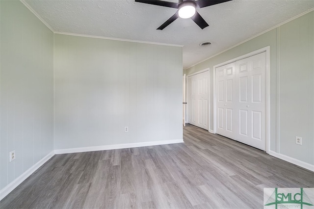 unfurnished bedroom featuring crown molding, light wood-type flooring, two closets, a textured ceiling, and ceiling fan