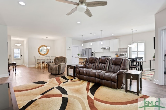 living room featuring light wood-type flooring and ceiling fan with notable chandelier