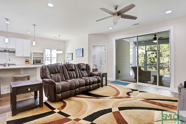 living room featuring ceiling fan, sink, and light wood-type flooring