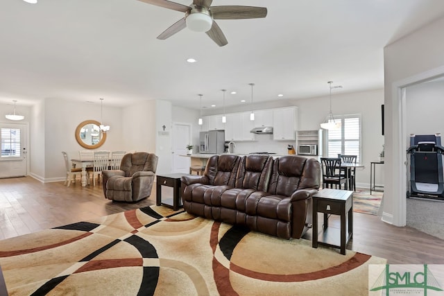 living room featuring ceiling fan with notable chandelier and light hardwood / wood-style floors