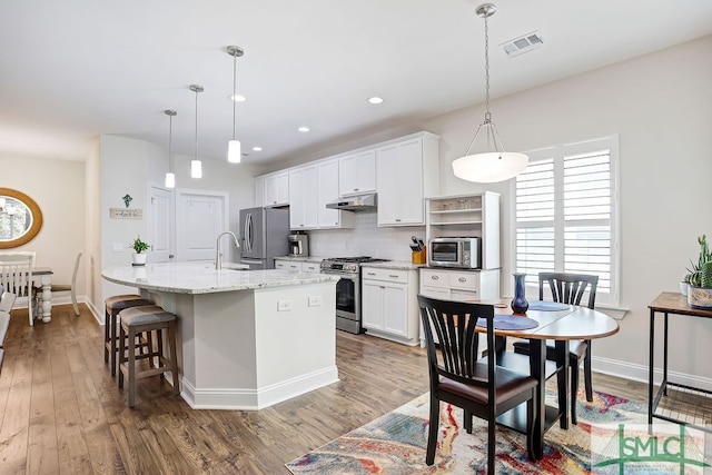 kitchen featuring white cabinetry, stainless steel appliances, pendant lighting, dark hardwood / wood-style floors, and a kitchen island with sink