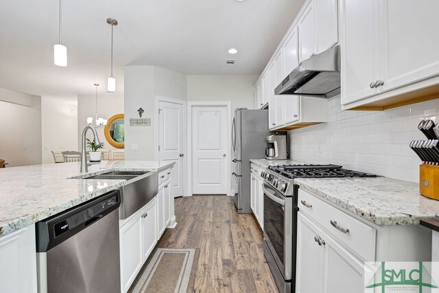 kitchen with white cabinets, hanging light fixtures, appliances with stainless steel finishes, wood-type flooring, and light stone counters