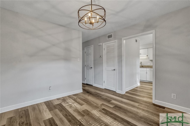 unfurnished room with sink, a chandelier, a textured ceiling, and light wood-type flooring