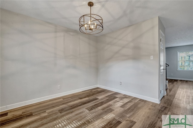 unfurnished dining area featuring an inviting chandelier, a textured ceiling, and hardwood / wood-style flooring