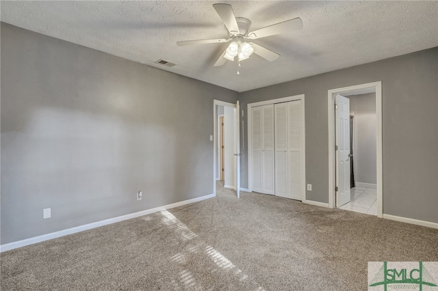 unfurnished bedroom with light carpet, a closet, a textured ceiling, and ceiling fan