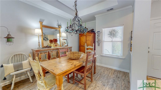 dining area with a tray ceiling, light hardwood / wood-style flooring, ornamental molding, and a notable chandelier