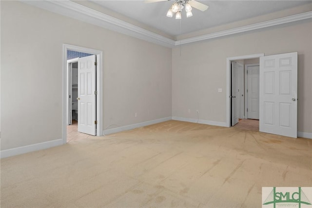 unfurnished bedroom featuring carpet flooring, baseboards, a spacious closet, a ceiling fan, and crown molding