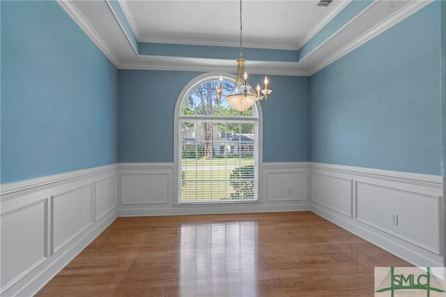 unfurnished dining area featuring a chandelier, a raised ceiling, wood finished floors, and a wainscoted wall