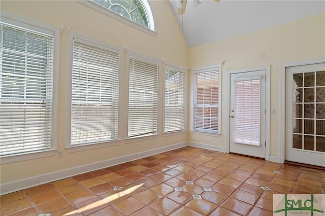 unfurnished sunroom with high vaulted ceiling, baseboards, and tile patterned flooring