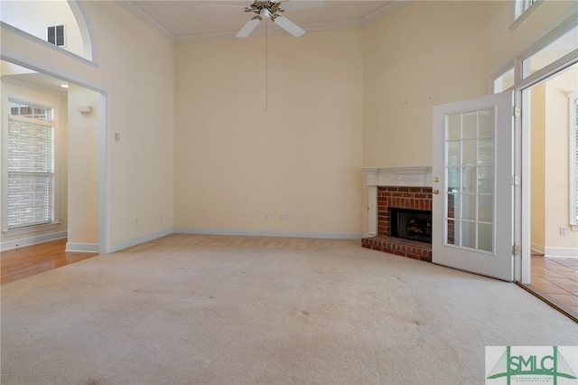 unfurnished living room featuring light carpet, a towering ceiling, ornamental molding, and a brick fireplace