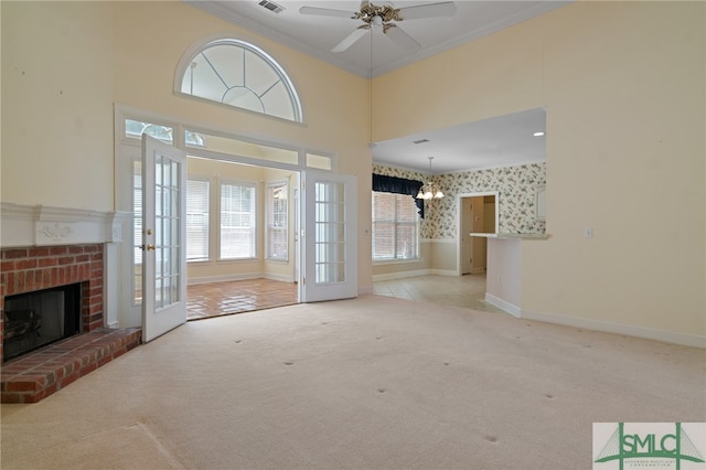 unfurnished living room with light carpet, crown molding, a towering ceiling, a fireplace, and ceiling fan with notable chandelier