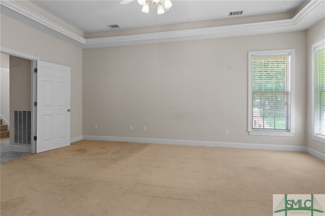 empty room featuring ornamental molding, light colored carpet, a tray ceiling, and ceiling fan