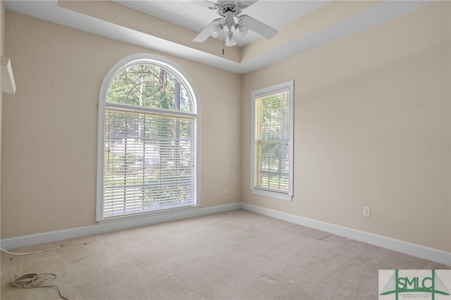 carpeted spare room with a raised ceiling, plenty of natural light, and ceiling fan