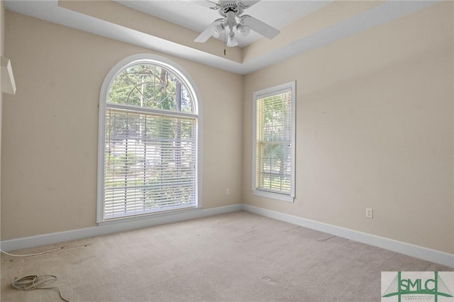 carpeted spare room with a tray ceiling, baseboards, and ceiling fan