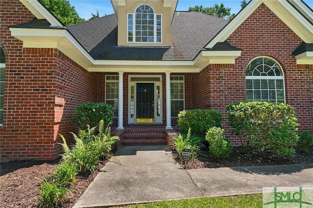 view of exterior entry featuring a shingled roof and brick siding