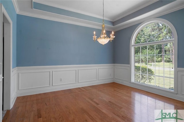 empty room featuring crown molding, a notable chandelier, a wainscoted wall, and wood finished floors