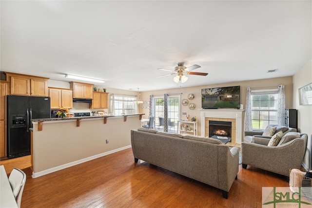 living room featuring a tile fireplace, ceiling fan with notable chandelier, and dark hardwood / wood-style flooring