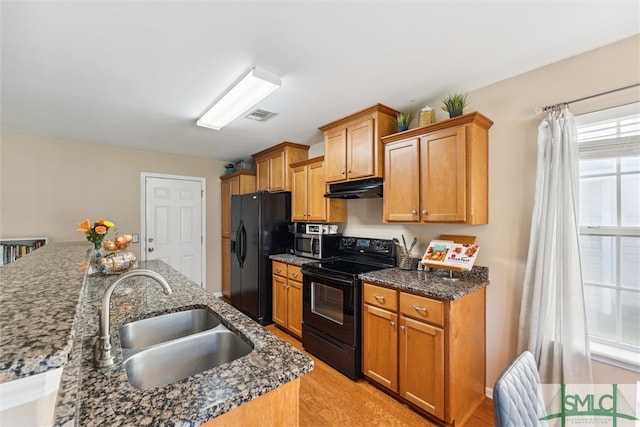 kitchen with sink, black appliances, light hardwood / wood-style flooring, and dark stone countertops