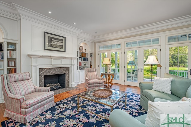 living room with wood-type flooring, a fireplace, built in shelves, crown molding, and french doors