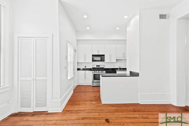 117 W Gaston St, Savannah, GA 31401 - kitchen with black microwave, dark countertops, gas stove, white cabinets, and light wood-style flooring