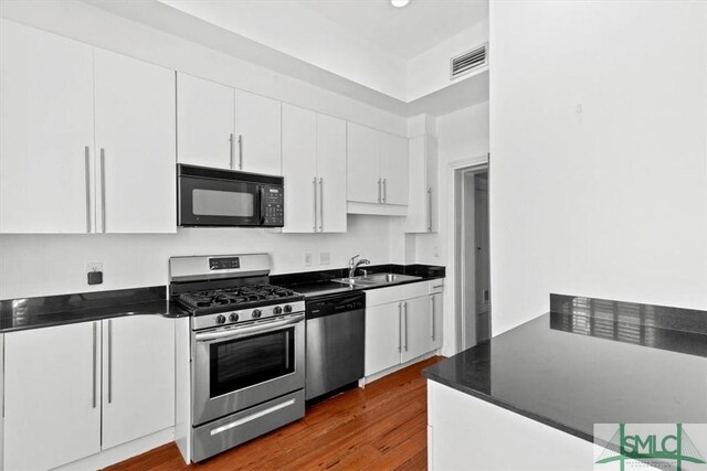 117 W Gaston St, Savannah, GA 31401 - kitchen with visible vents, dark wood-type flooring, white cabinets, a sink, and appliances with stainless steel finishes