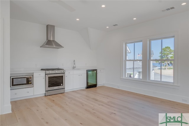 kitchen featuring appliances with stainless steel finishes, sink, light wood-type flooring, and wall chimney range hood